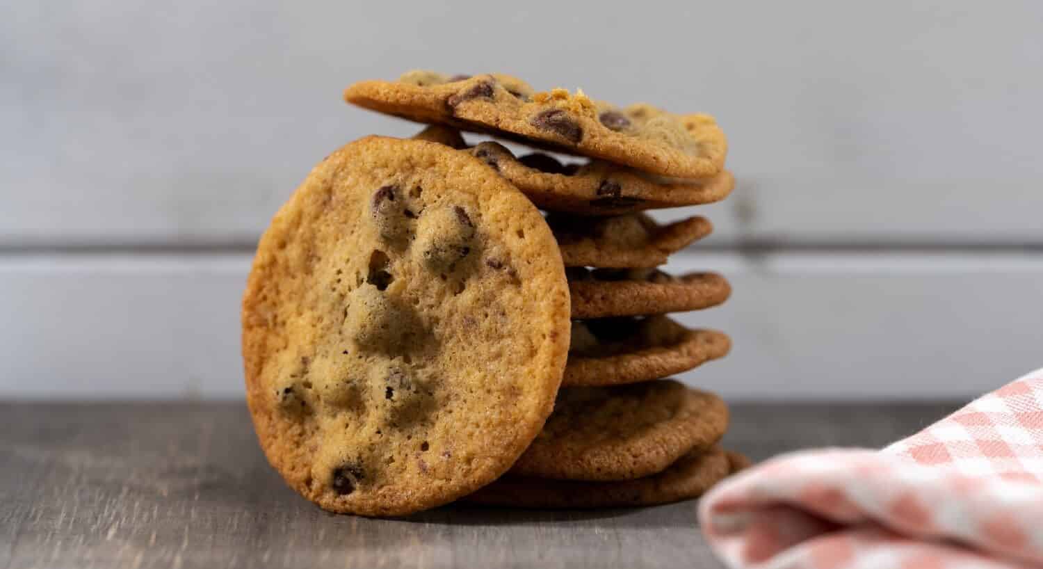 A tower of fresh golden brown chocolate chip cookies next to a pink and white checkered towel