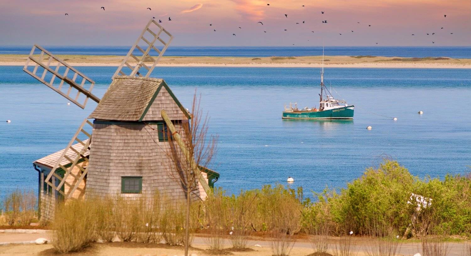 Brown windmill at waters edge with a fishing boat in the water nearby