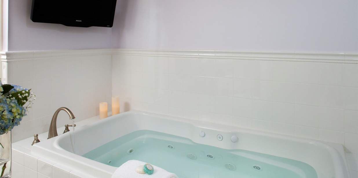 A large, white jetted tub in a bathroom. The tub is filled with water, and candles are on the side, creating a relaxing atmosphere.