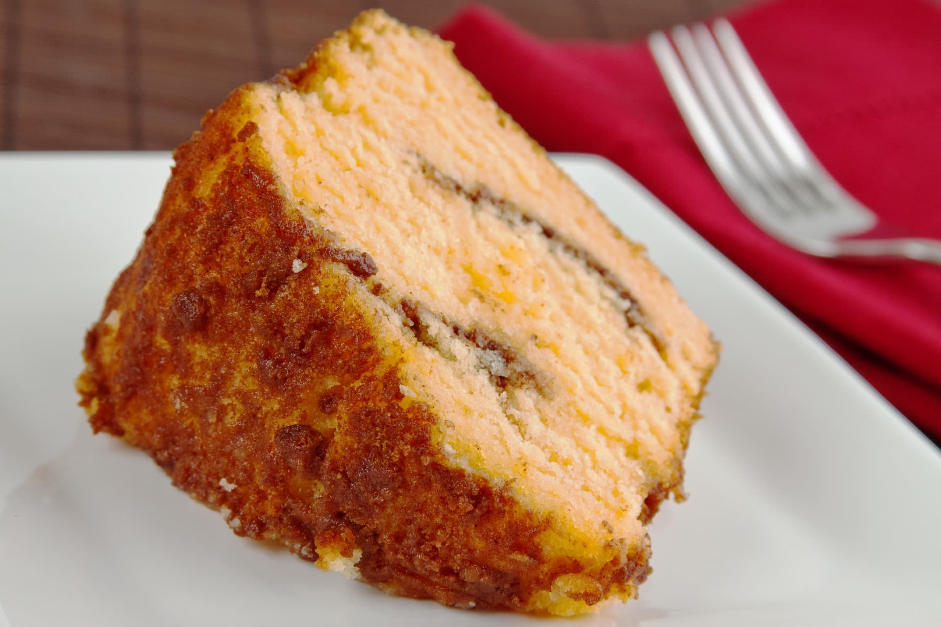A slice of layered cake on a white plate with a red napkin in the background.