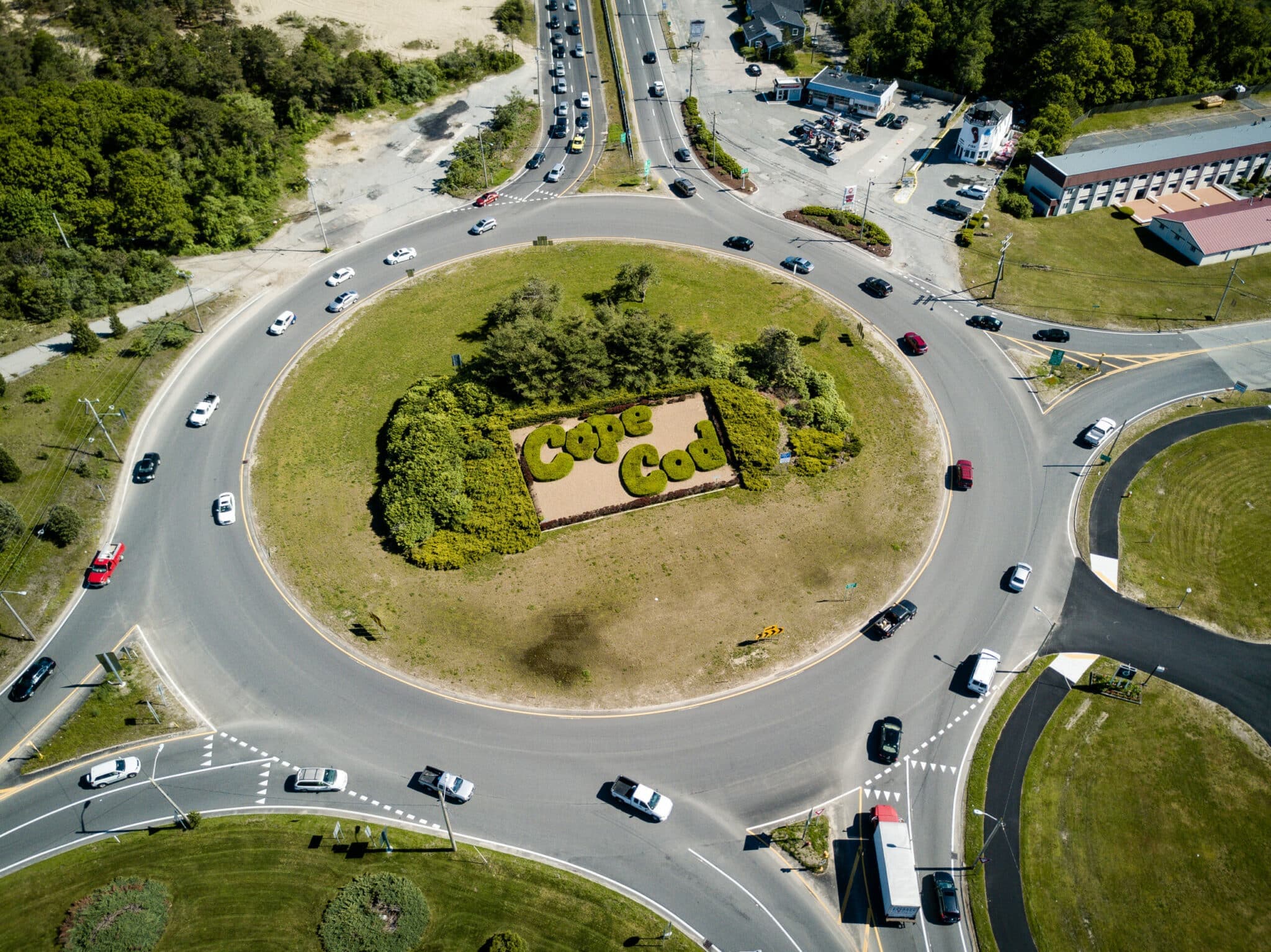 Aerial view of a roundabout with a landscaped "Cape Cod" sign surrounded by cars.