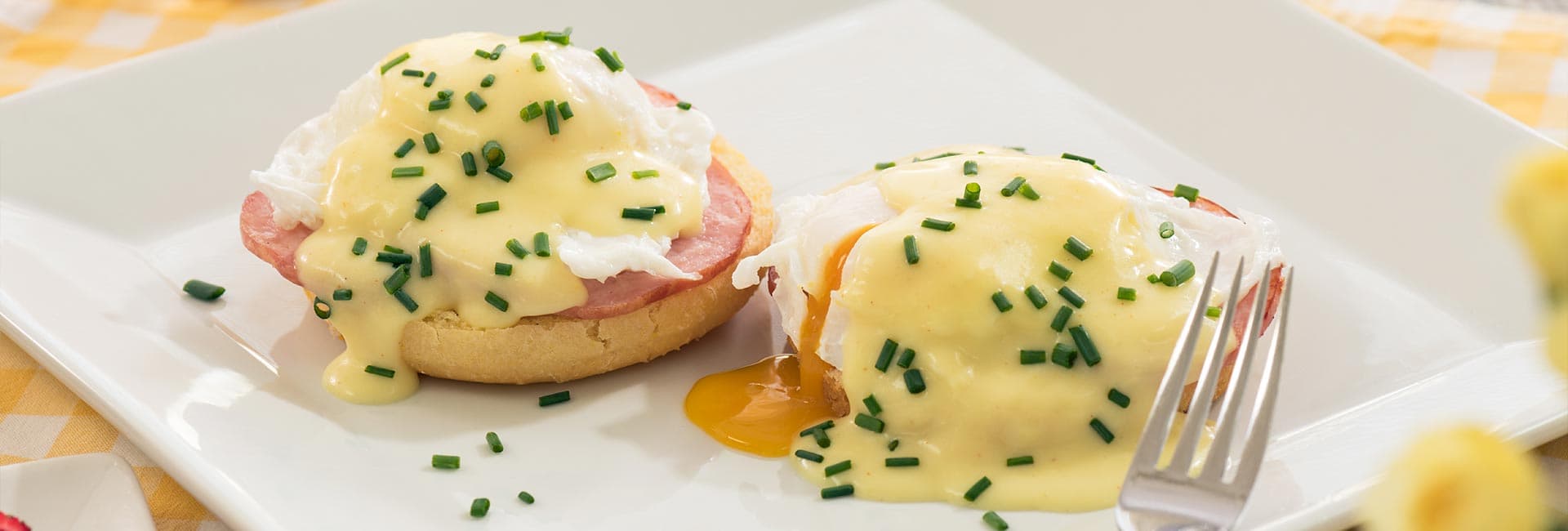 Two eggs Benedict topped with hollandaise sauce and chives on English muffins.