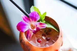 A refreshing cocktail garnished with a purple flower and mint in a copper cup.