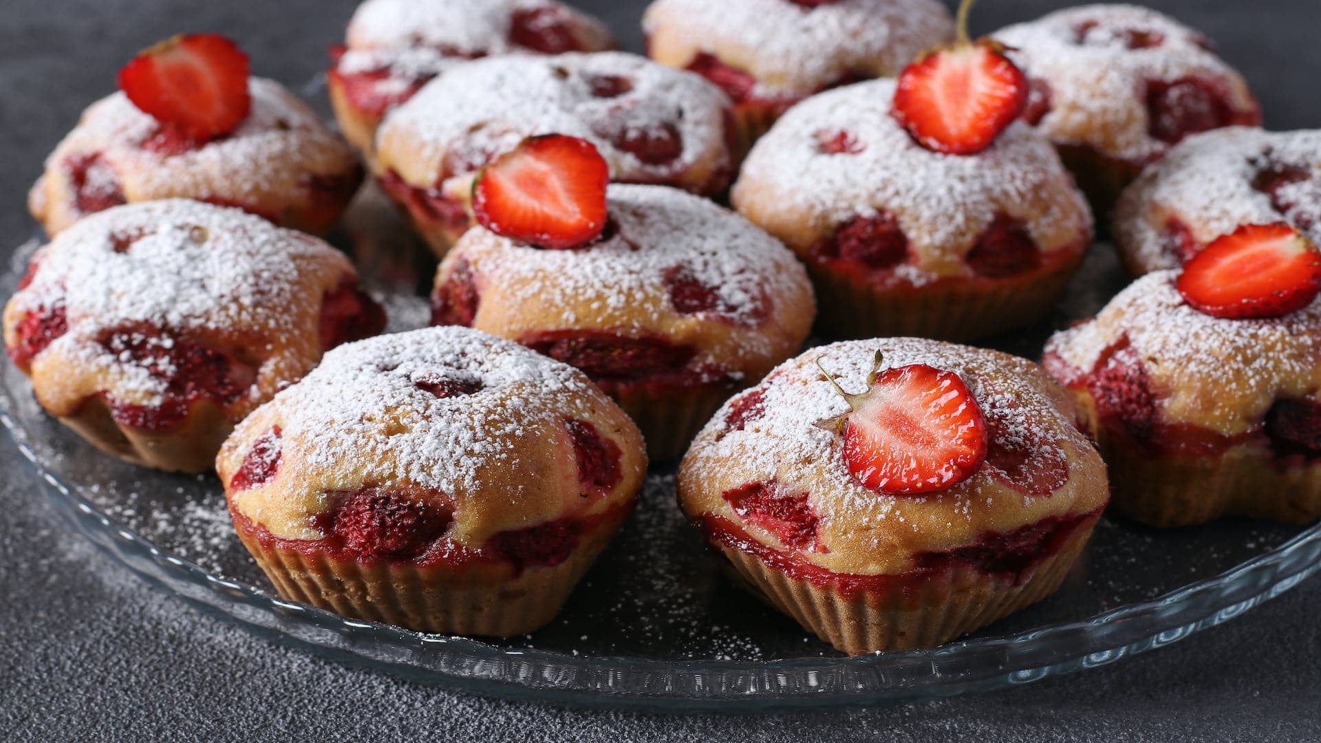A plate of freshly baked strawberry muffins dusted with powdered sugar.