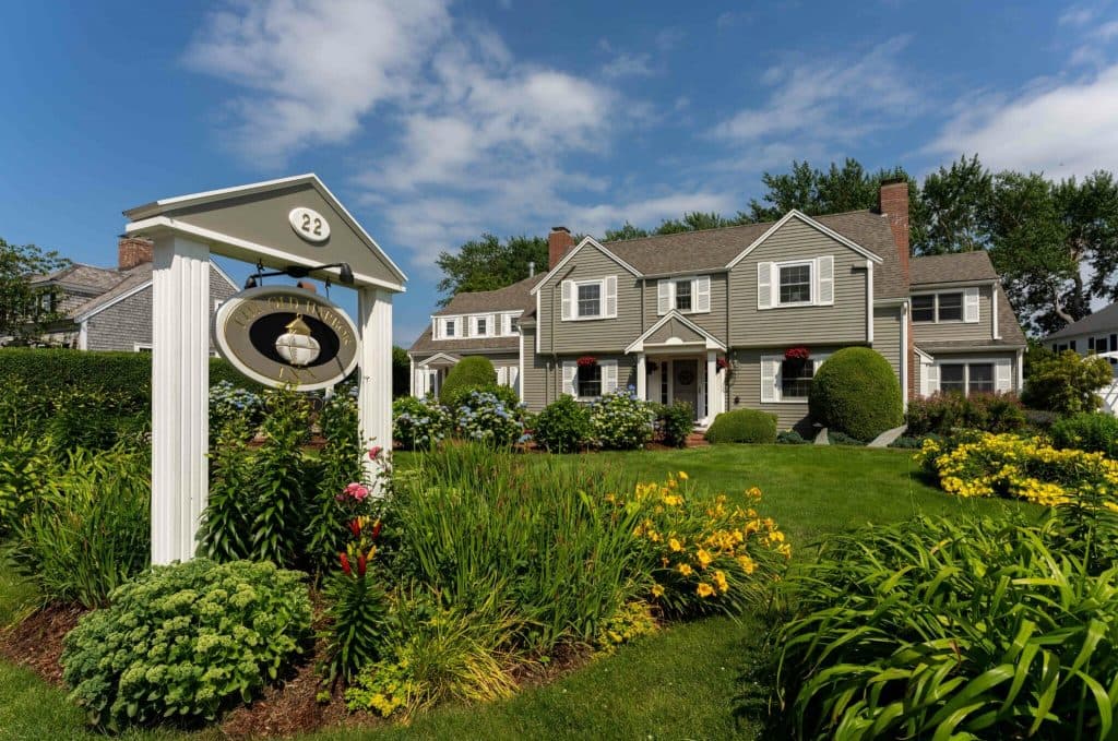 A charming two-story house with a green exterior surrounded by colorful gardens and a sign displaying the number 22.