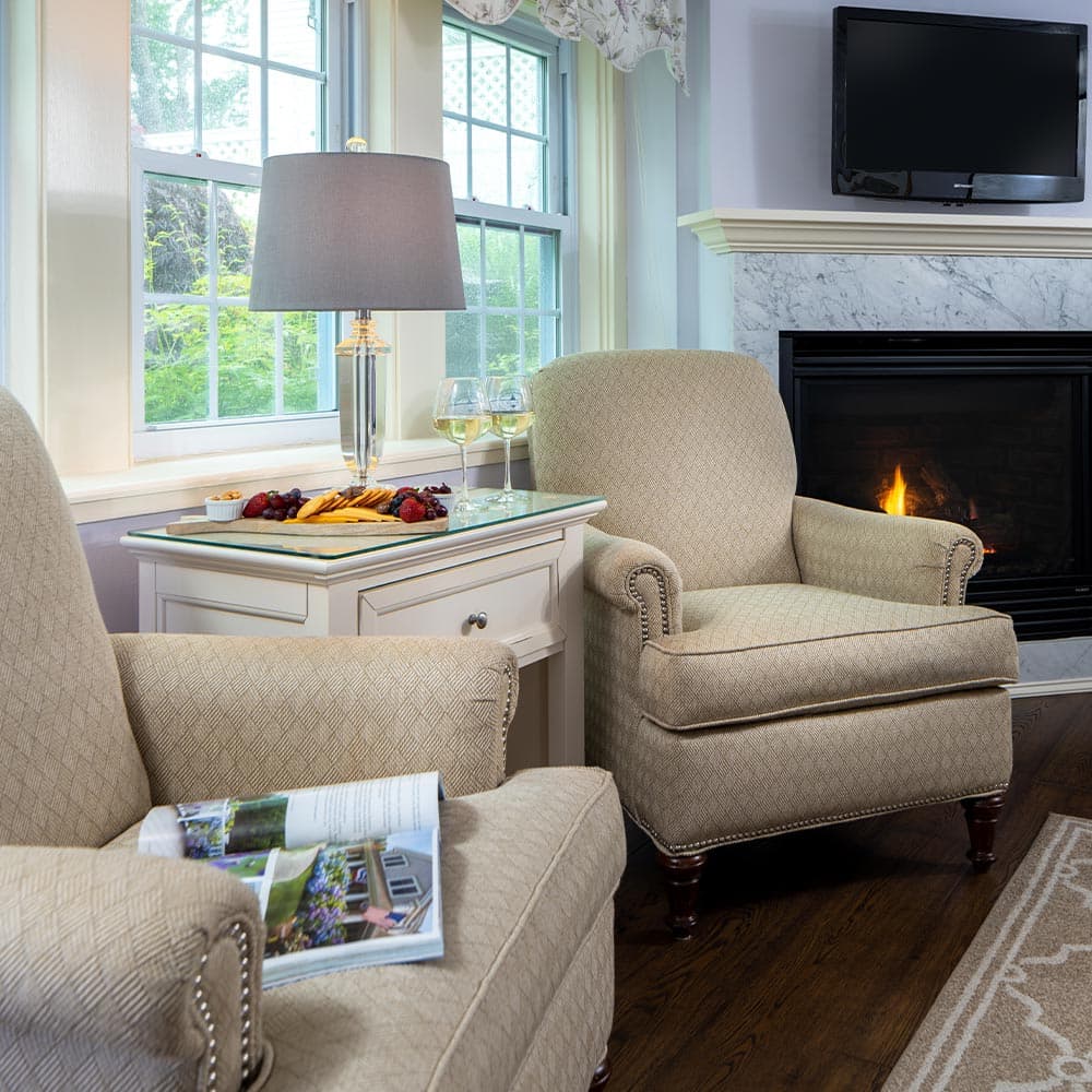 Cozy living room with two armchairs, a lamp, a snack tray with wine glasses, and a fireplace.