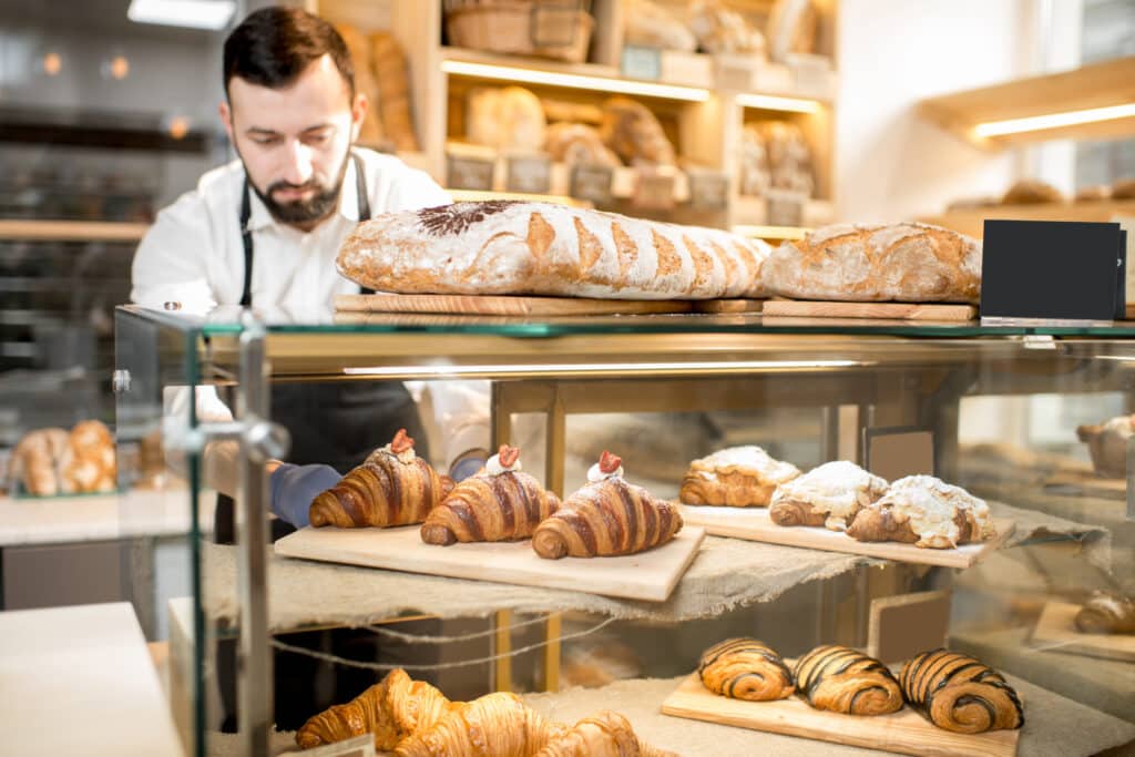 A baker arranges a variety of freshly baked pastries in a display case.