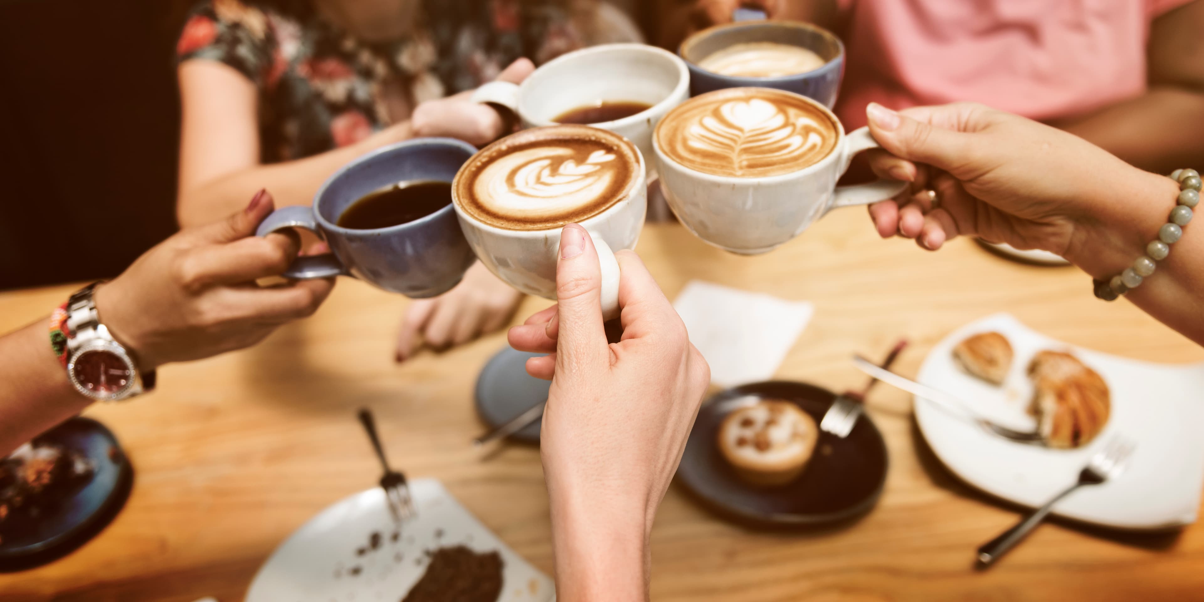 A group of people clinking coffee cups together on a wooden table. A group of people clinking coffee cups together on a wooden table.