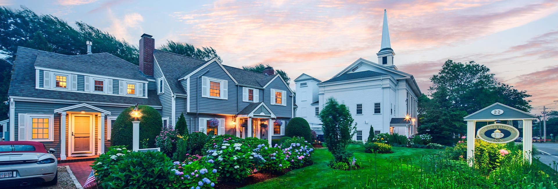 A charming house with flower gardens and a church tower at sunset.