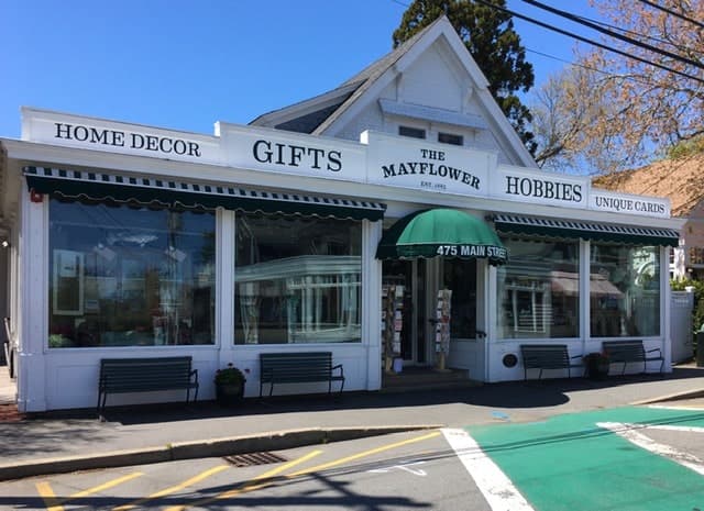 A white storefront with green accents displaying signs for home decor, gifts, hobbies, and unique cards.