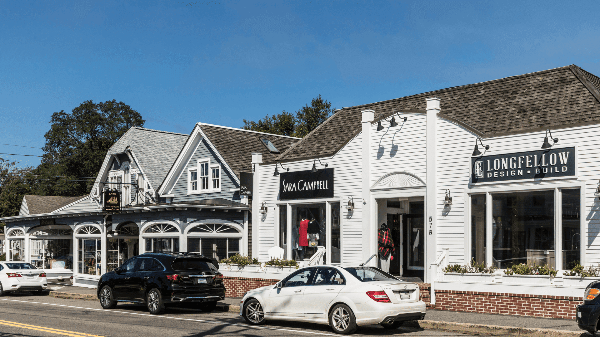 A street view of charming storefronts, including Sara Campbell and Longfellow Design & Build, with parked cars in front. A street view of charming storefronts, including Sara Campbell and Longfellow Design & Build, with parked cars in front.