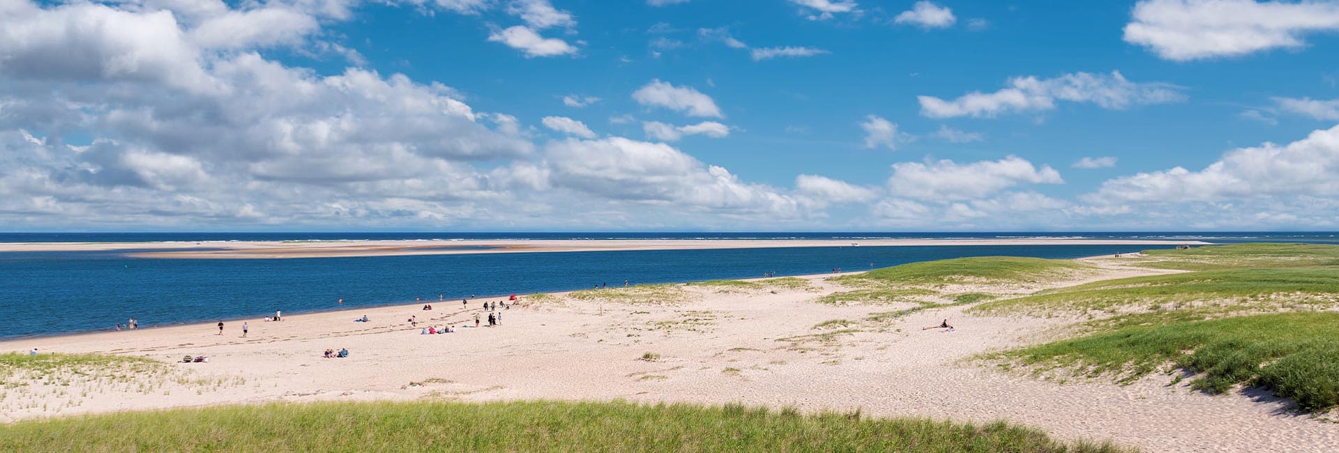 A sandy beach stretches along a calm blue sea under a partly cloudy sky.