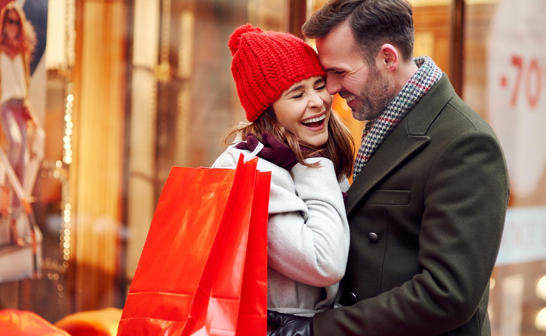A joyful couple embraces while holding shopping bags in a festive setting.