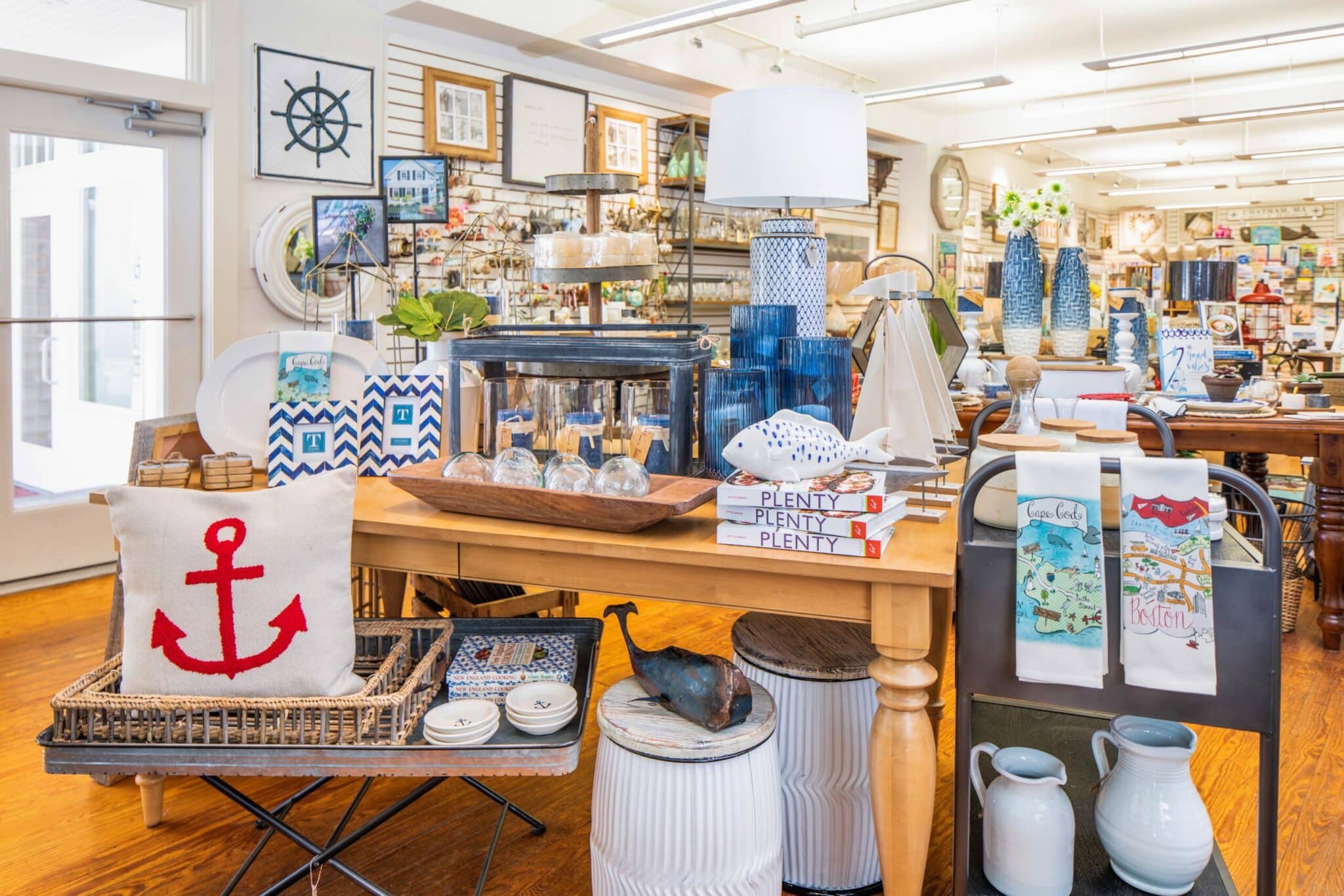 A cozy home goods store displaying nautical-themed decor and various kitchen items on wooden tables.