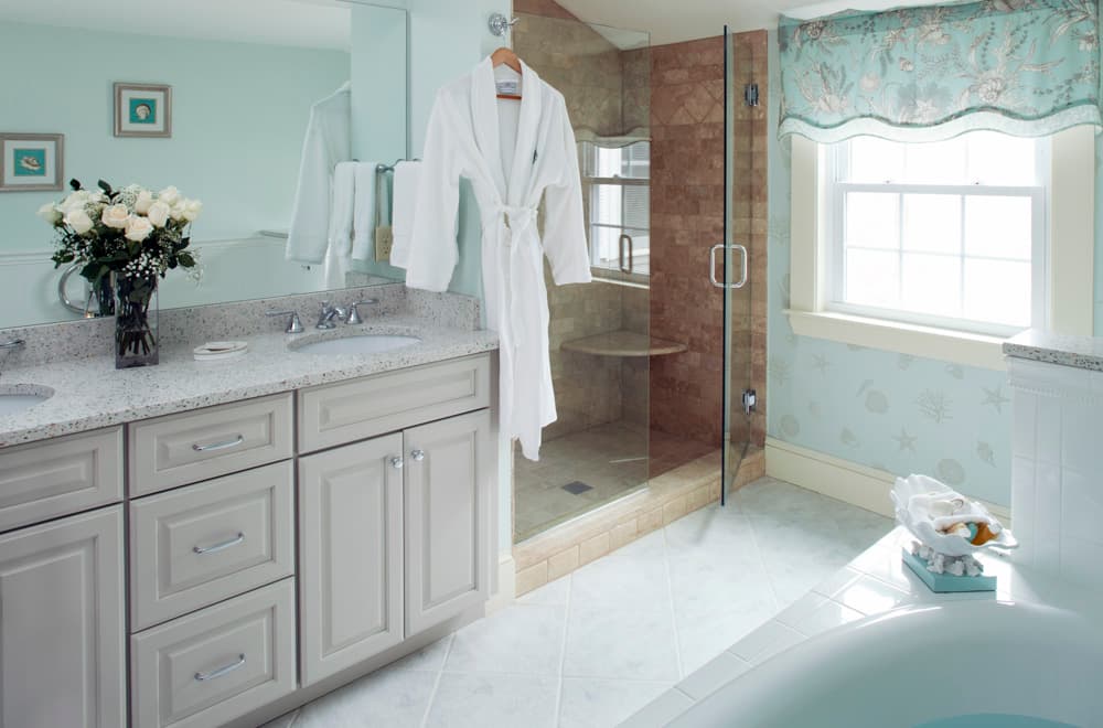 A stylish bathroom featuring a glass shower, a sink with a granite countertop, and a white robe hanging nearby.