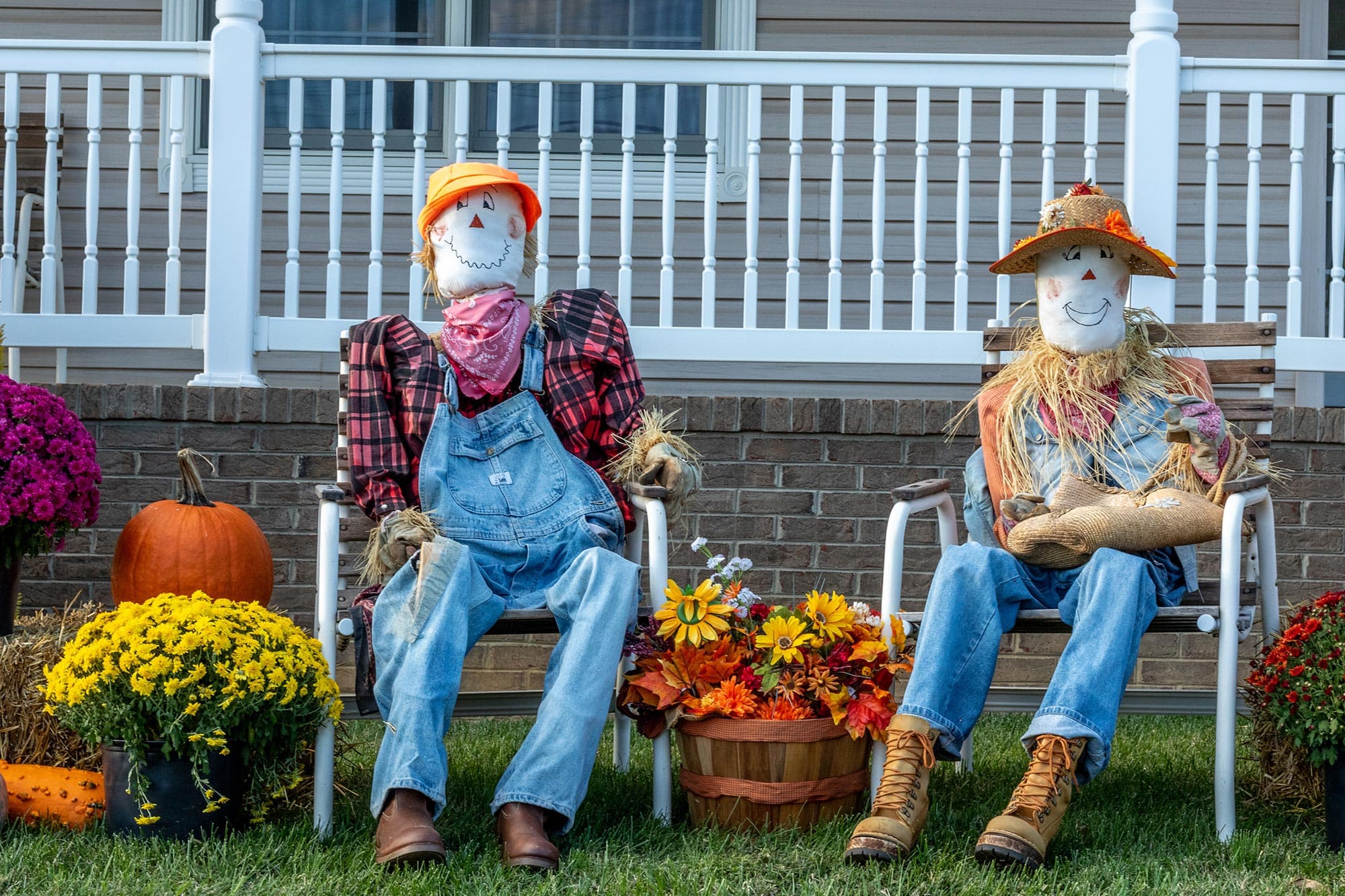 Two colorful scarecrows sit on lawn chairs surrounded by pumpkins and flowers. Two colorful scarecrows sit on lawn chairs surrounded by pumpkins and flowers.