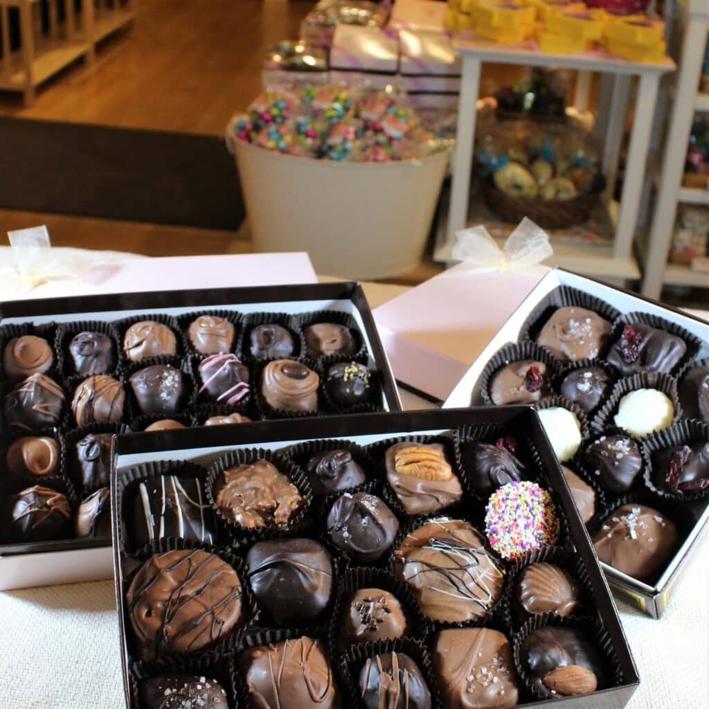 A display of assorted chocolate truffles in decorative boxes, set against a background of candy jars.