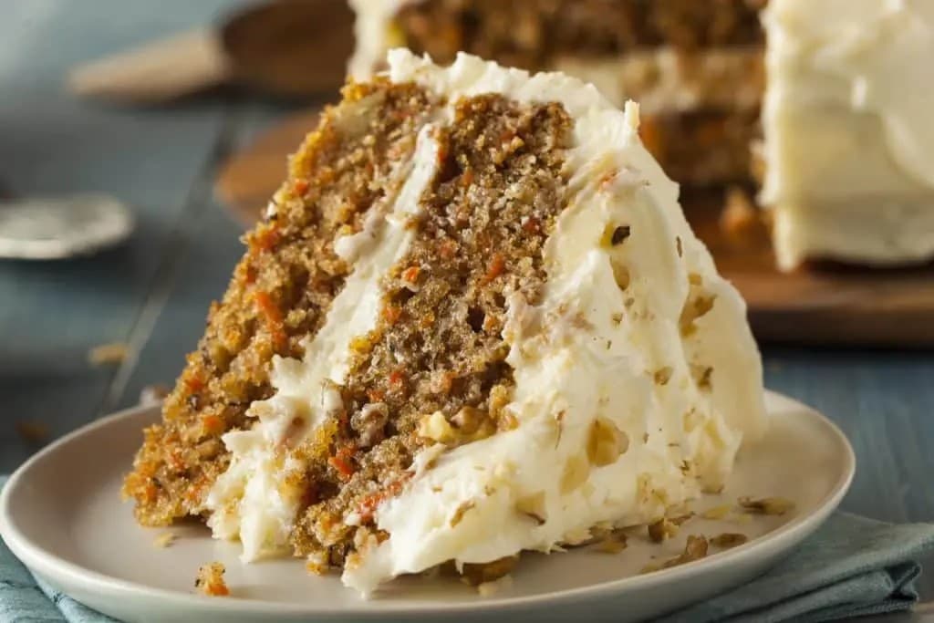 A slice of carrot cake with cream cheese frosting on a plate.