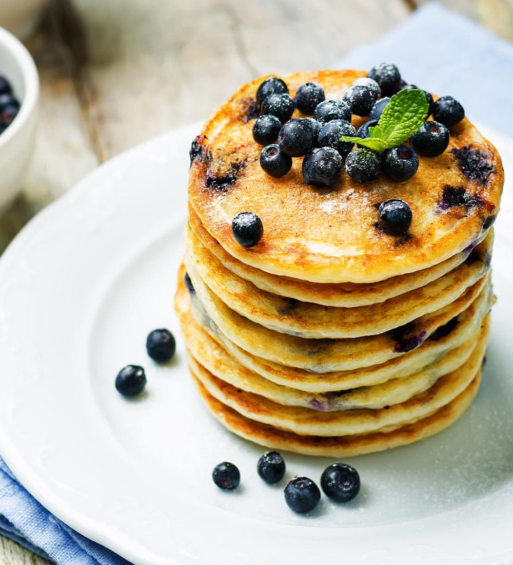 A stack of golden pancakes topped with fresh blueberries and a sprig of mint.