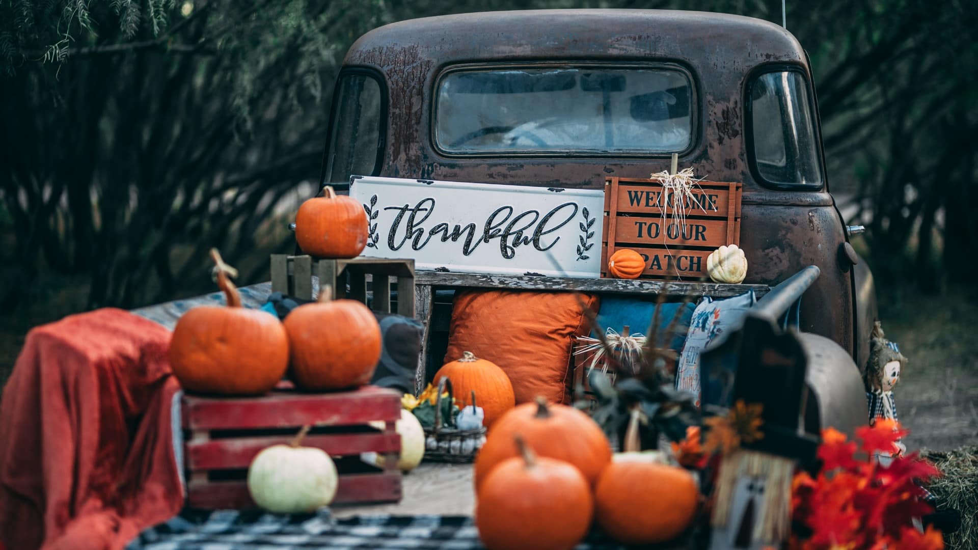 A rustic truck loaded with pumpkins and autumn decorations, featuring a sign that reads "thankful."