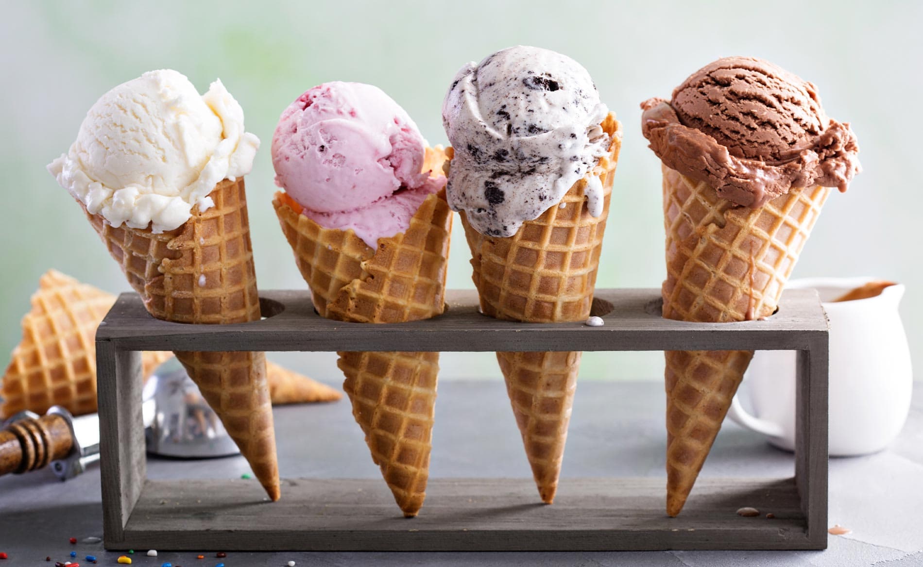 Four ice cream cones in a wooden holder, featuring vanilla, strawberry, cookies and cream, and chocolate flavors.