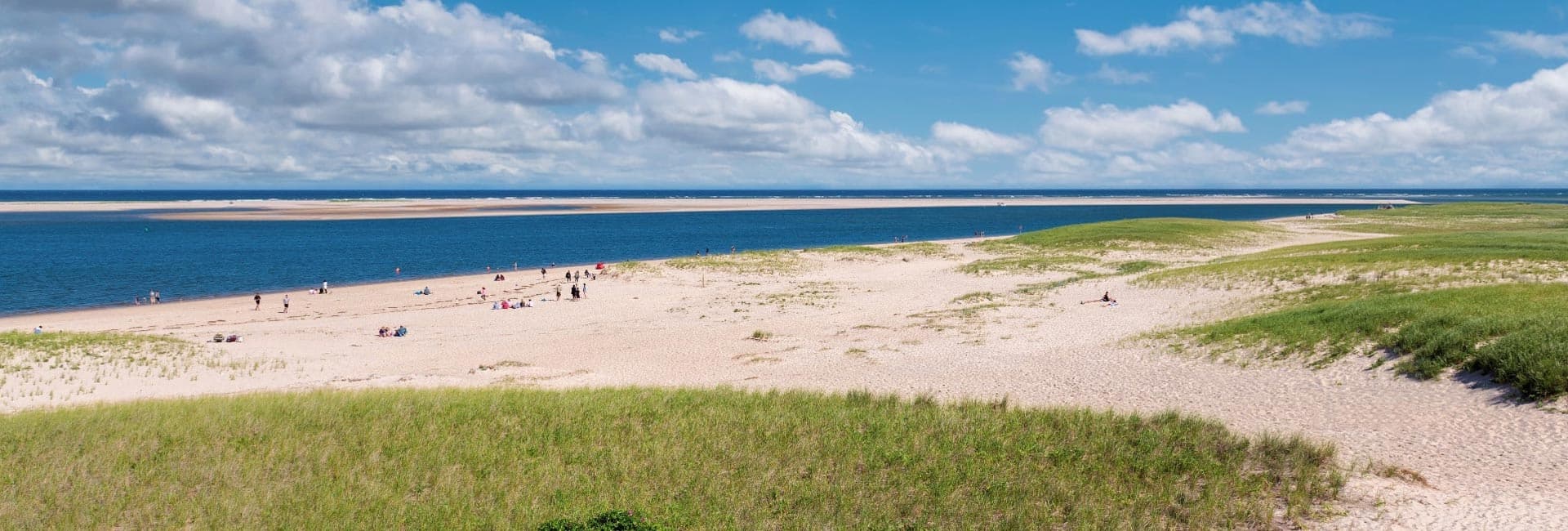 A scenic beach with sandy dunes and a calm blue sea under a partly cloudy sky.
