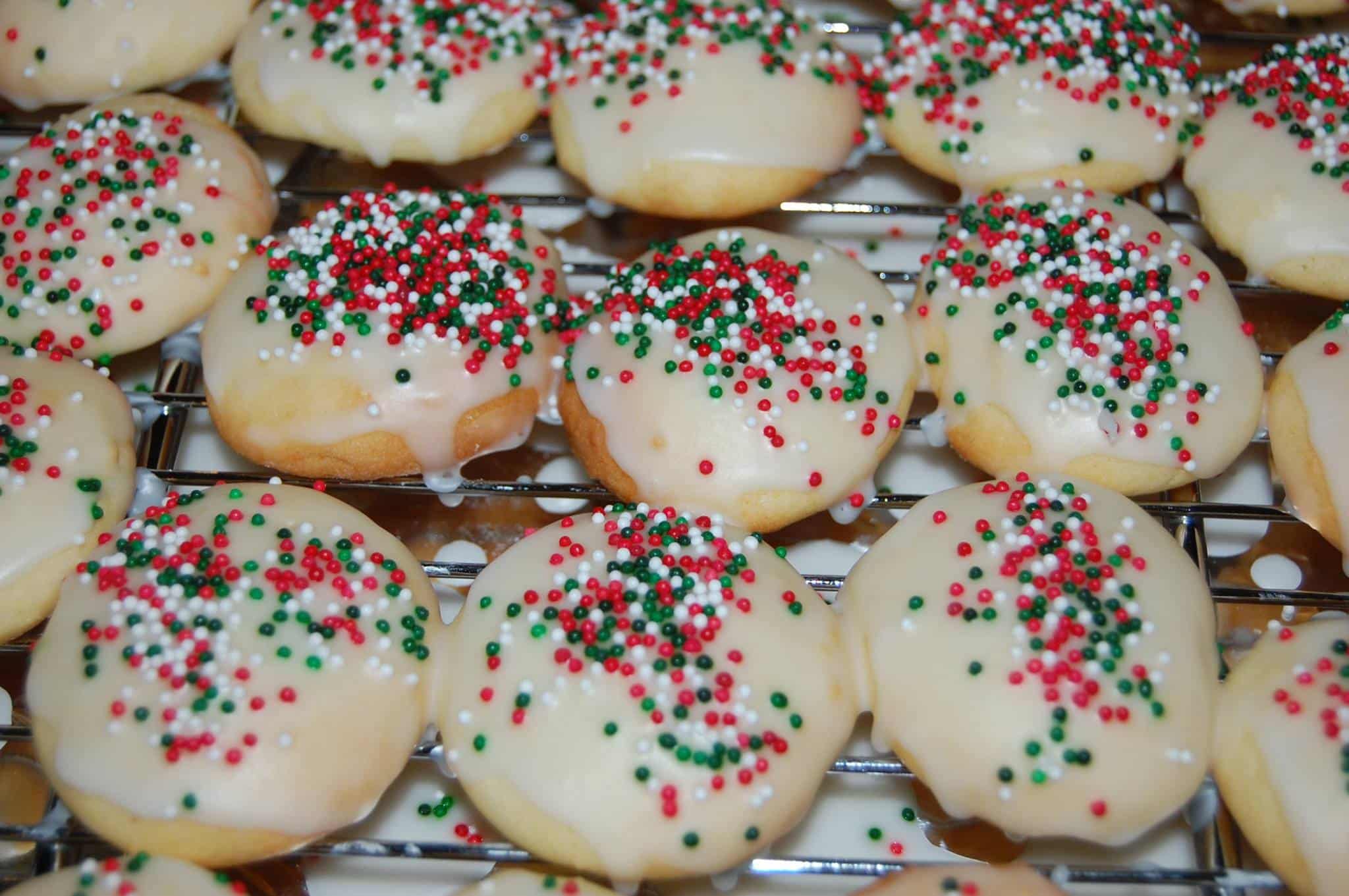 A close-up of frosted cookies topped with red and green sprinkles on a cooling rack.