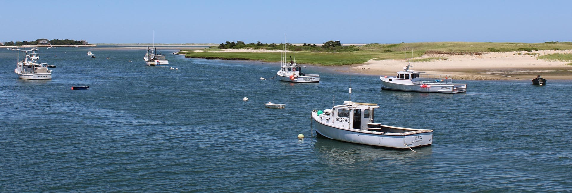 A serene waterway with several fishing boats anchored near a sandy shore and green vegetation.