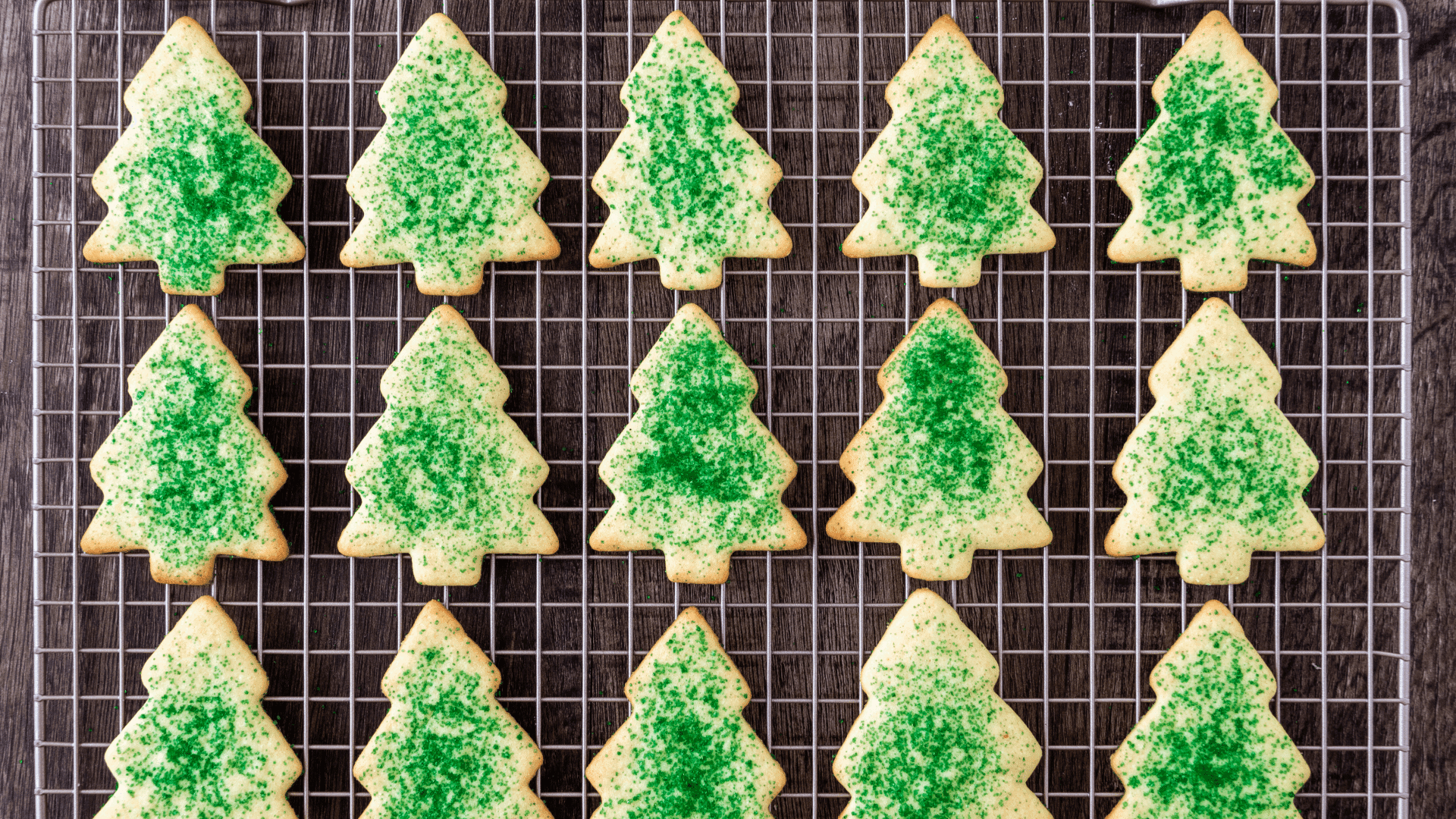 A cooling rack filled with green-sprinkled Christmas tree-shaped cookies.