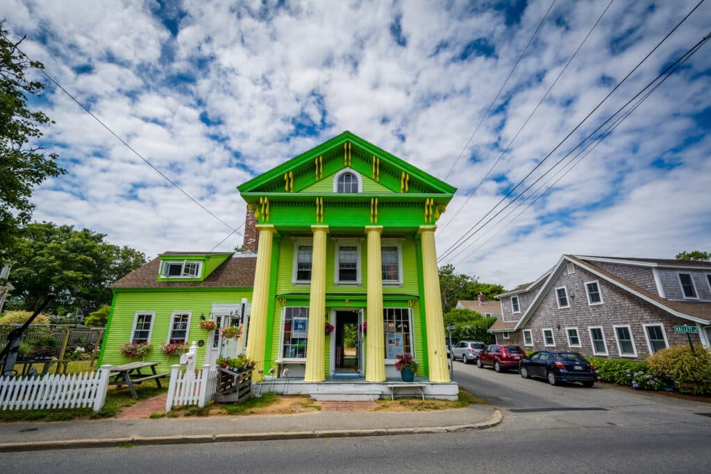 A vibrant green house with white columns stands on a cloudy day, surrounded by other buildings.