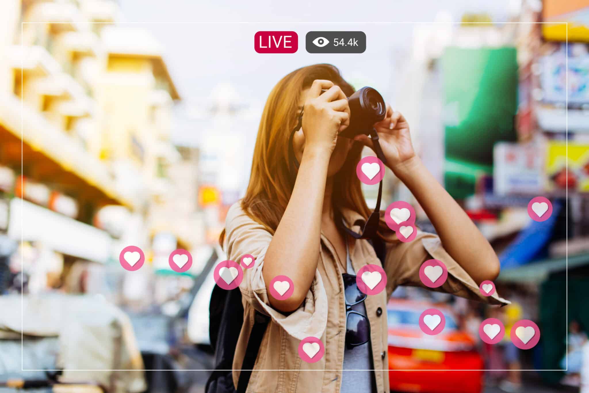 A person with long hair holds a camera in a busy street, surrounded by animated heart icons.