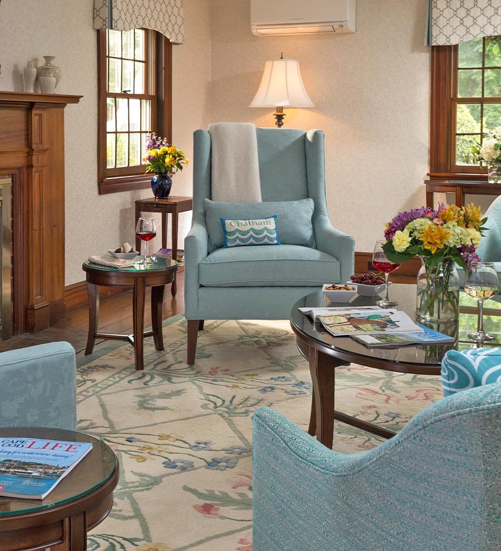 A cozy living room featuring a blue armchair, a small table with drinks and snacks, and floral decor.