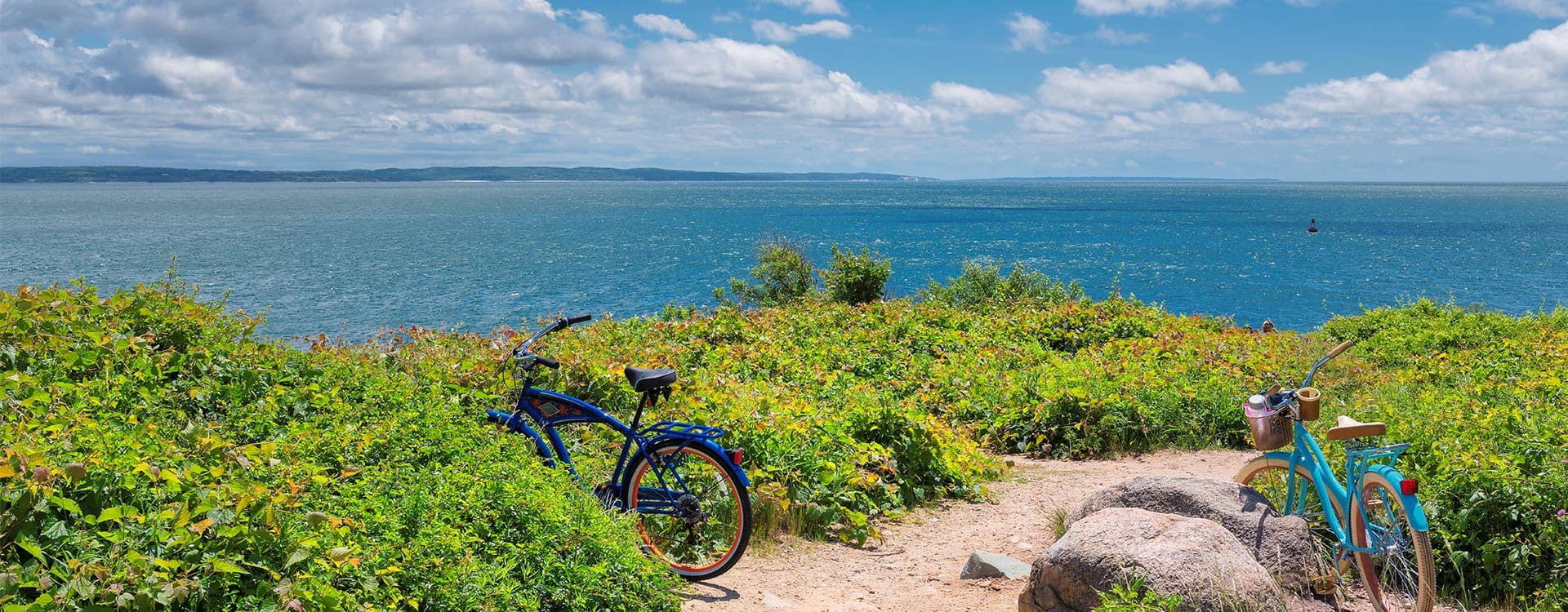 Two bicycles are parked near a grassy area overlooking the ocean under a partly cloudy sky.