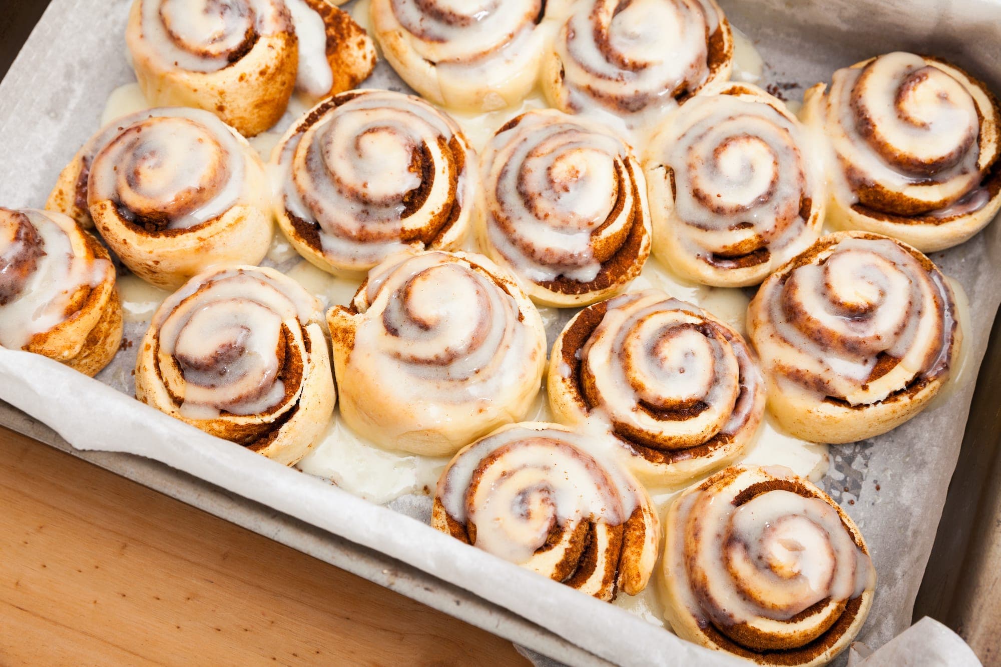 A tray of freshly baked cinnamon rolls drizzled with icing.