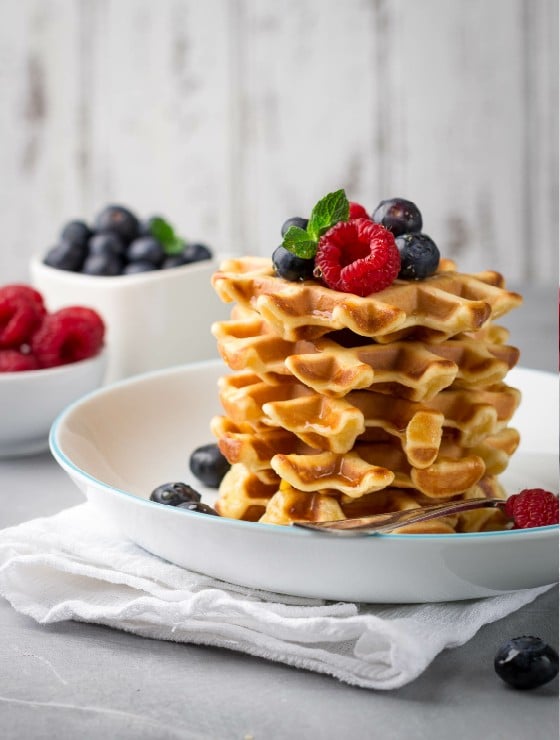 Waffles stacked on top pf echa other topped with raspberries and blrries