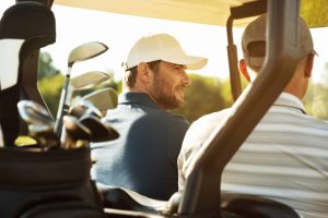 Two male golfers sitting in a cart and talking