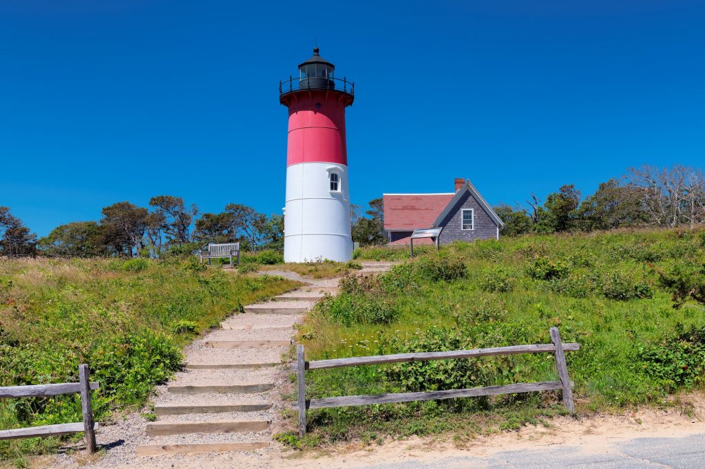 Lighthouse half read half white up a hill with stairs 