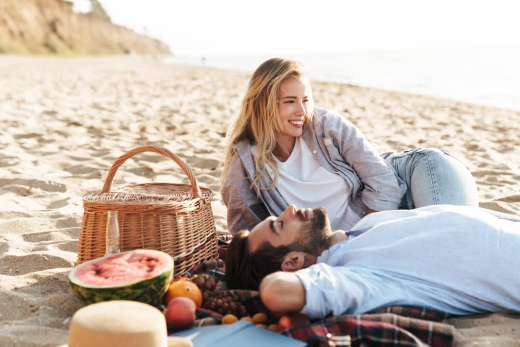 Lovely young couple having a picnic at the beach, laughing