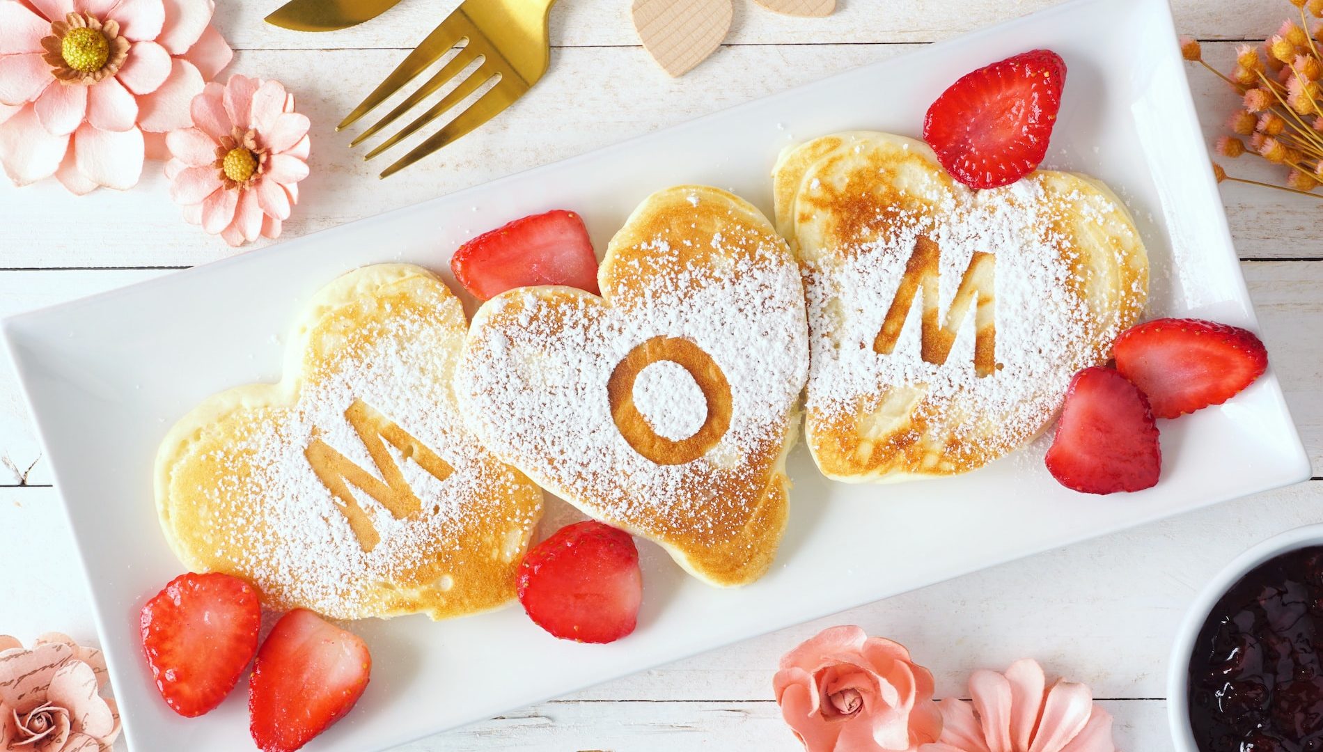 Heart shaped pancakes with MOM letters. Mothers Day breakfast concept. Top view table scene with a white wood background.