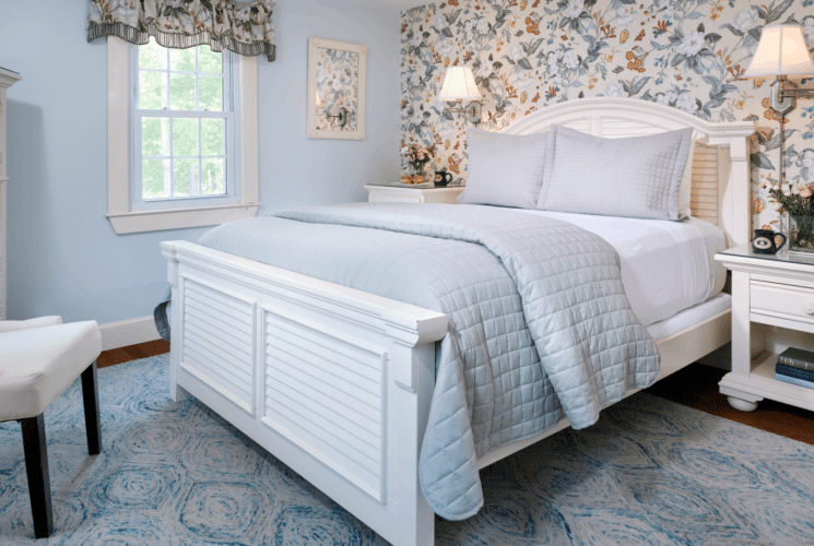 Elegant bedroom with floral wallpaper, queen bed, sitting chairs and window