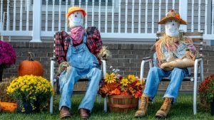 Scarecrows in front of a house sitting on chairs 