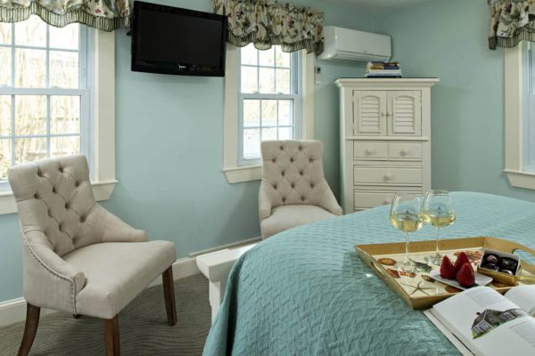 Light blue guest room, several windows, flat screen tv, armoire and two sitting chairs