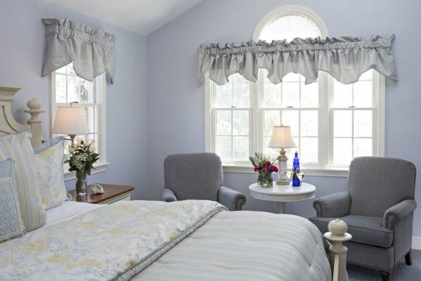 Blue guest room with vaulted ceilings, several windows, upholstered chairs and cozy bed