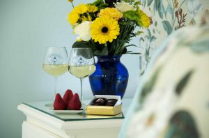 Fresh flowers in a vase, two wine glasses with wine, and a box of chocolates