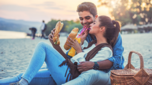 Happy couple enjoying a sandwich picnic on the beach 