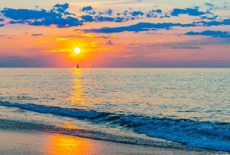 The shoreline of a beach with a small surf cresting at dusk