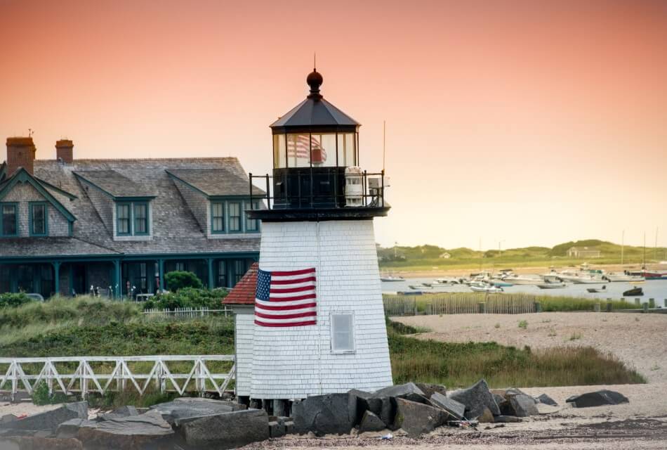 White lighthouse on the beach with large building and water in the background