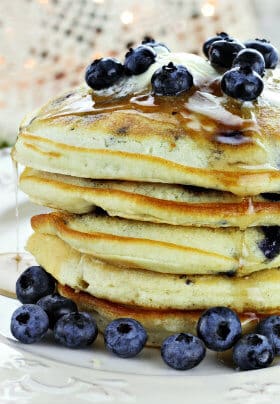 Tall stack of golden brown pancakes topped with maple syrup and bleuberries