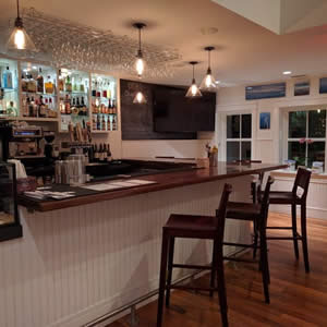 White paneled bar with stained top, barstools, pendant lights, and a variety of colorful bottles