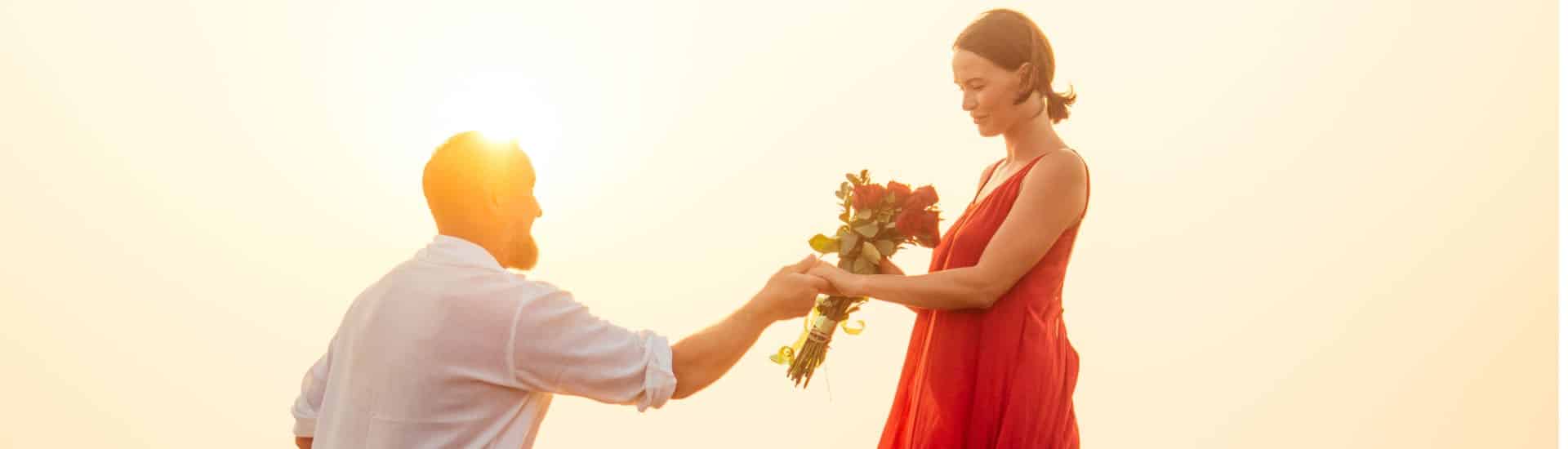 A man in a white shirt proposing to a girl in a red dress holding red roses